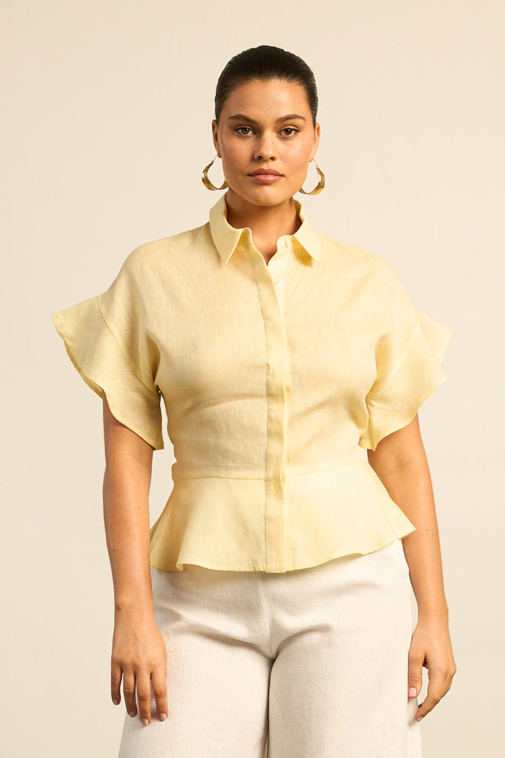 Woman wearing a light yellow blouse with ruffled sleeves on a beige background