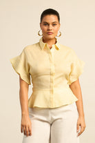 Woman wearing a light yellow blouse with ruffled sleeves on a beige background