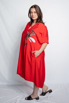Woman wearing a v neck bright red midi length dress with elbow length sleeves and  flower motif against a white background.
