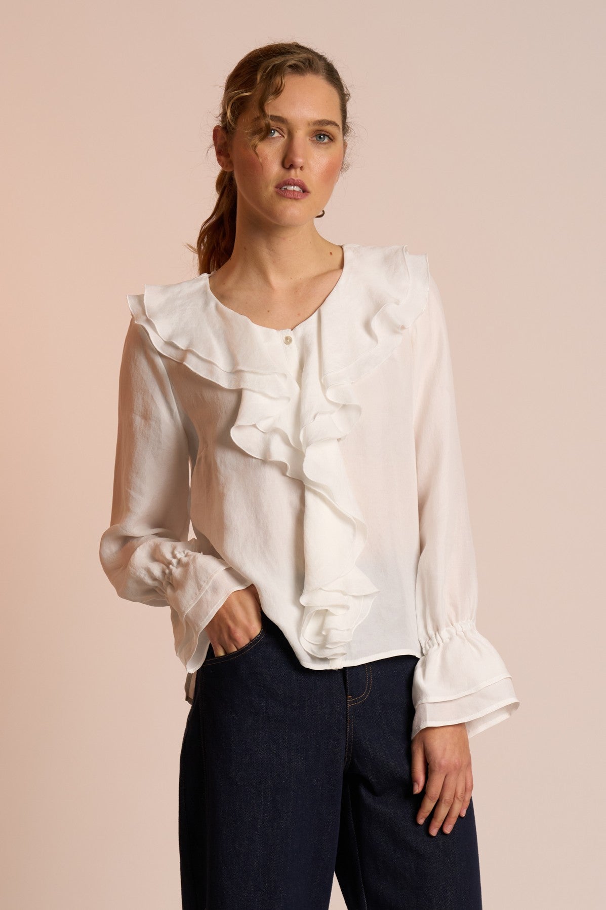 Woman wearing a white blouse with ruffled details on a beige background
