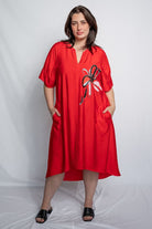 Woman wearing a v neck bright red midi length dress with elbow length sleeves and  flower motif against a white background.