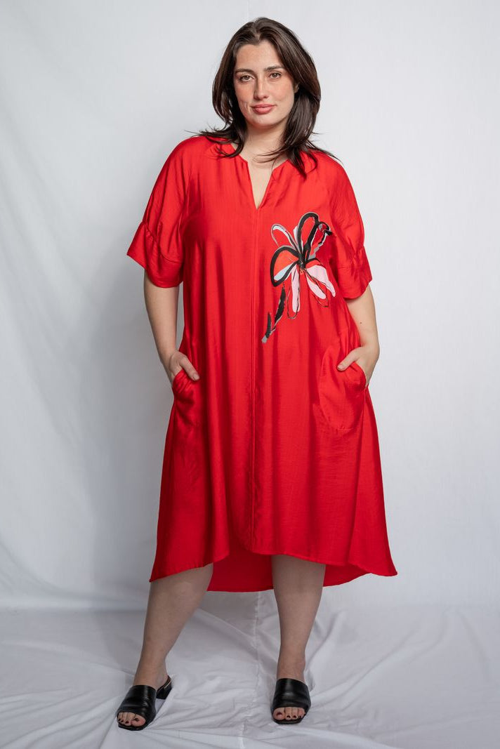 Woman wearing a v neck bright red midi length dress with elbow length sleeves and  flower motif against a white background.