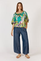 Woman wearing a colorful blouse and blue pants on a white background