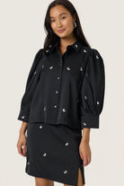 Woman wearing a black outfit with decorative elements on a plain background