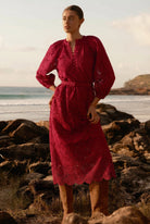 Woman in a red dress standing on a rocky beach with ocean and sky in the background
