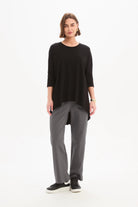 women wearing a black top and grey pants on a plain background