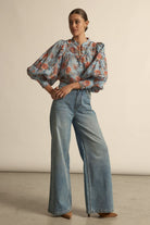Woman wearing a floral blouse and blue jeans against a beige background