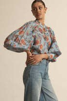 Woman wearing a floral blouse with puffed sleeves and jeans on a beige background